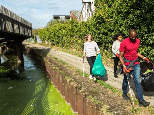 Three people man and two women litter picking along urban canal